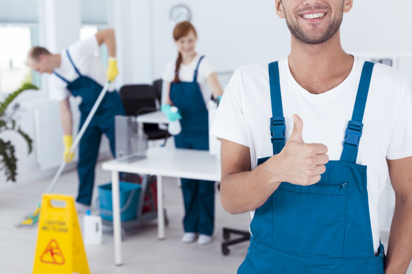 67708469 - smiling worker showing his thumb up and his friends working in the background